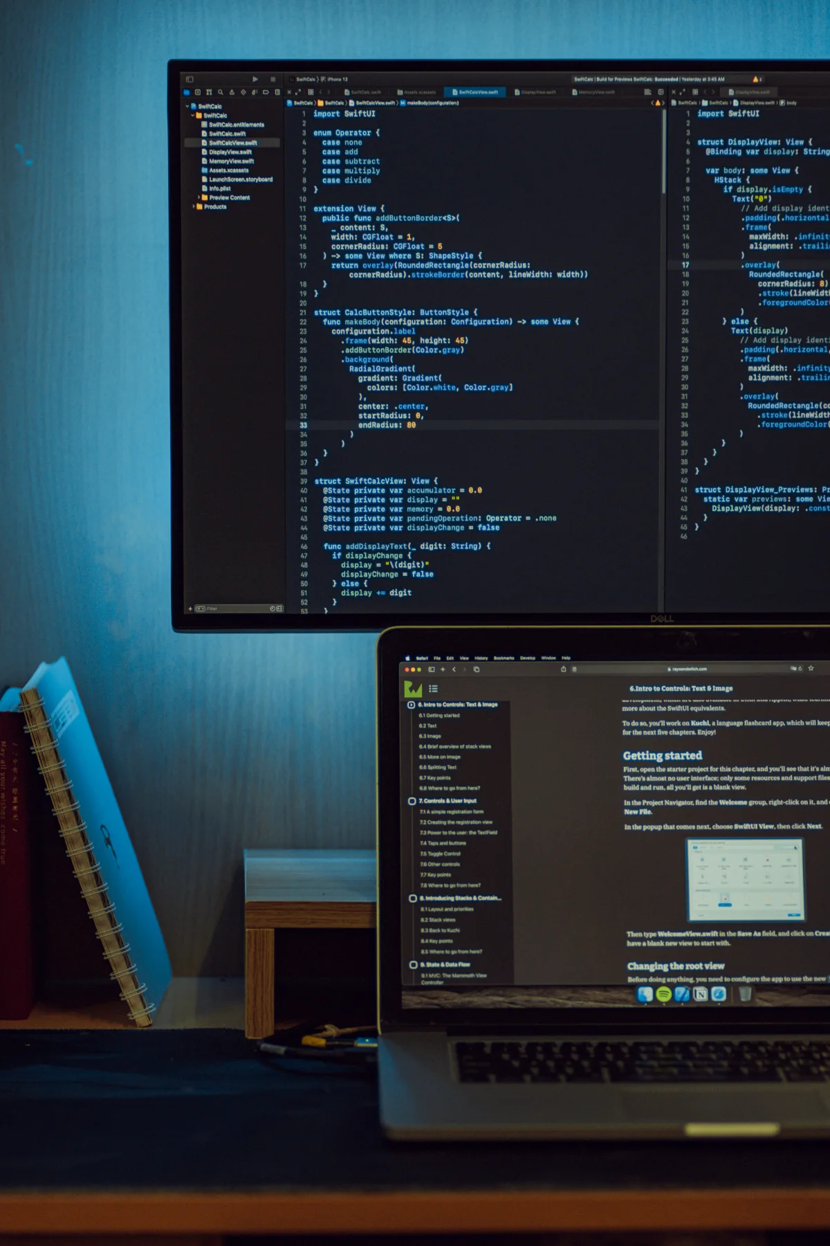 A blue-lit development workspace with code on a monitor and laptop